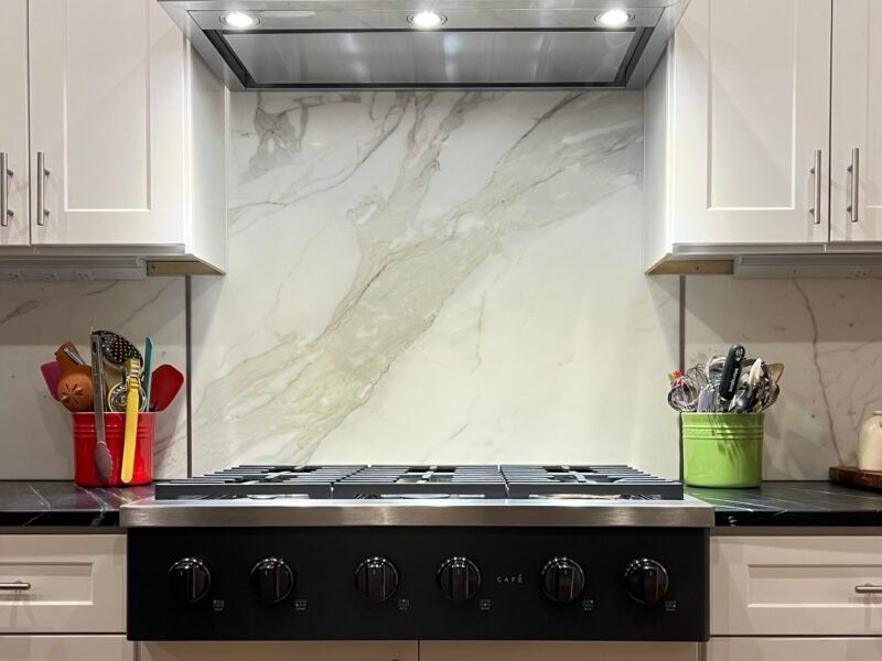 IMG_5111 Kitchen stove with marble backsplash, white cabinets, and cooking utensils.