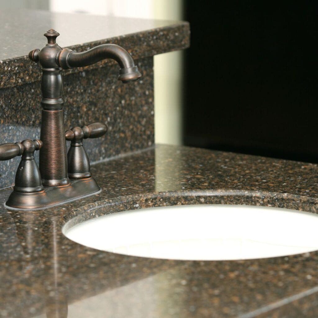 Bronze faucet and handles on a dark granite countertop with a white oval sink.