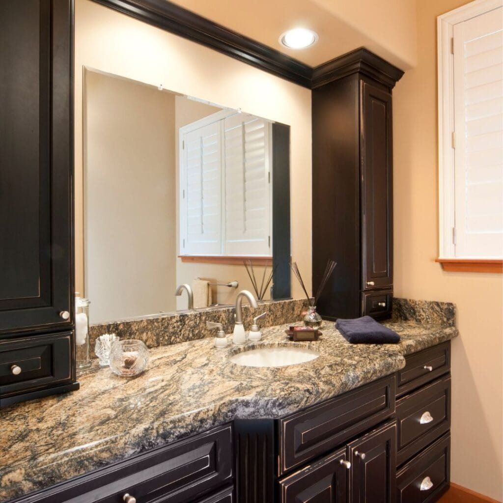 Bathroom vanity with dark cabinets, granite countertop, and large mirror.