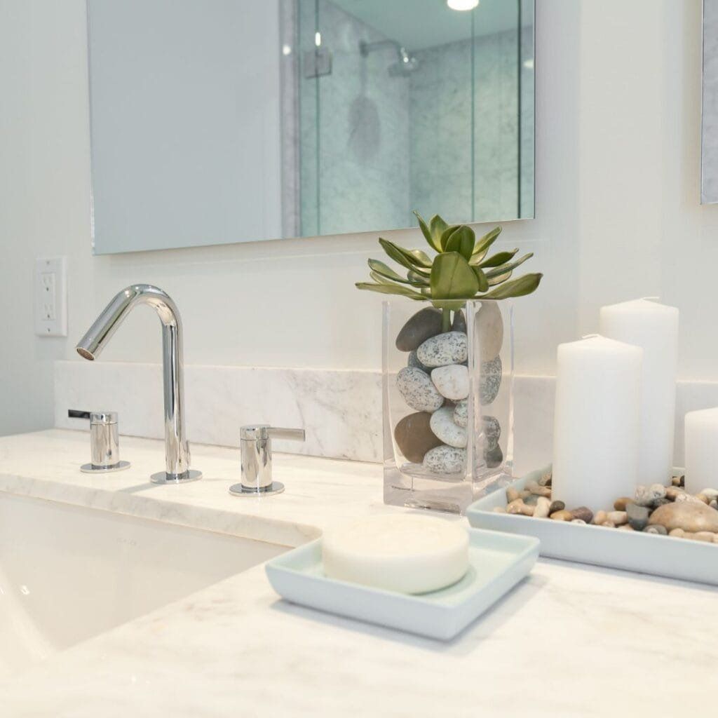Bathroom counter with a faucet, soap dish, candles, and decorative rocks and plants.