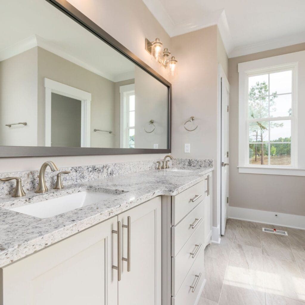 Bathroom with double vanity, large mirror, granite countertop, light fixtures, and window.