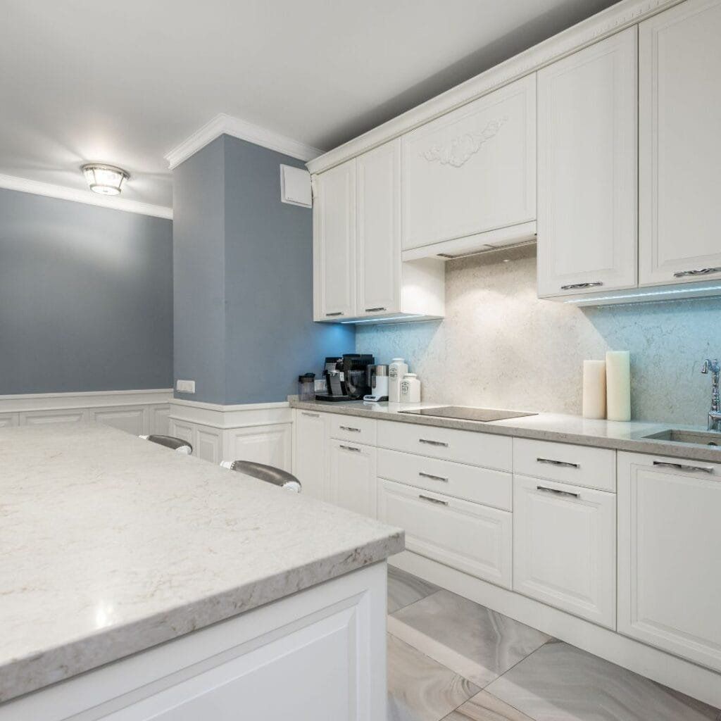 White kitchen with light marble countertop and cabinets; light blue accent wall.