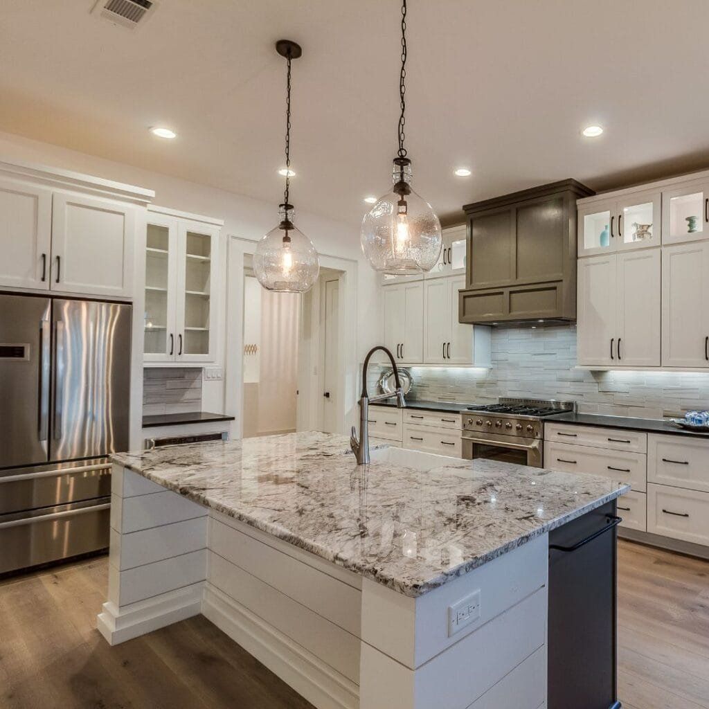 Spacious white kitchen with island, stainless steel appliances, pendant lights, and granite countertops.