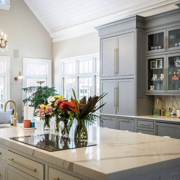 Gray and white kitchen with island, cabinets, marble countertops, and floral arrangements.