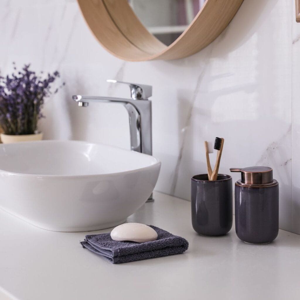 White bathroom sink with faucet, toiletries, and lavender against a marble wall.