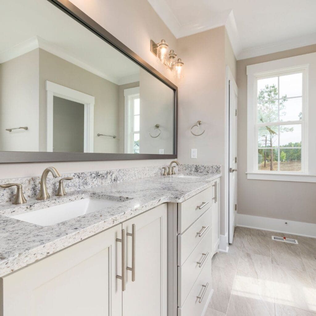 Bathroom with double sinks, large mirror, granite countertop, light cabinets, and a window.
