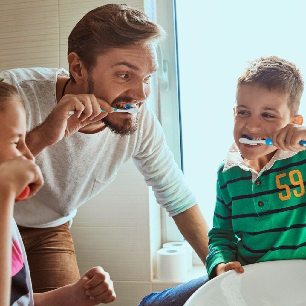 Father and two children brushing teeth in a bathroom.