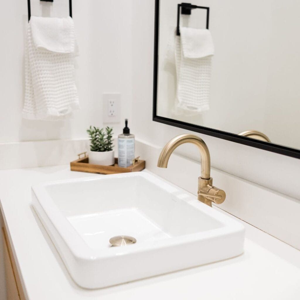 Modern bathroom with a white rectangular sink, gold faucet, and a black-framed mirror.
