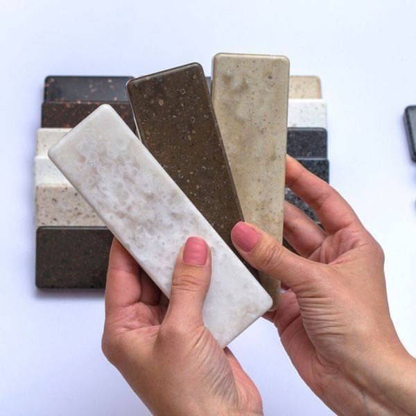 Hands holding and displaying several stone tile samples in various colors.
