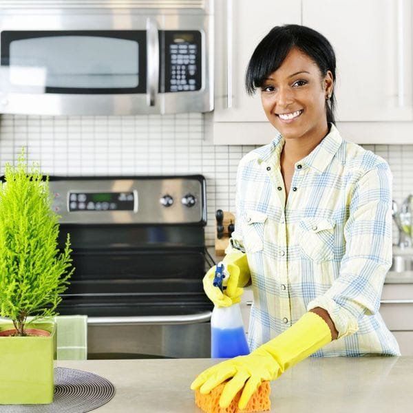 Woman cleaning kitchen counter with sponge and spray bottle.