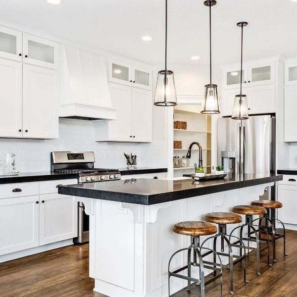 White kitchen with black countertops and island, pendant lights, and wood bar stools.