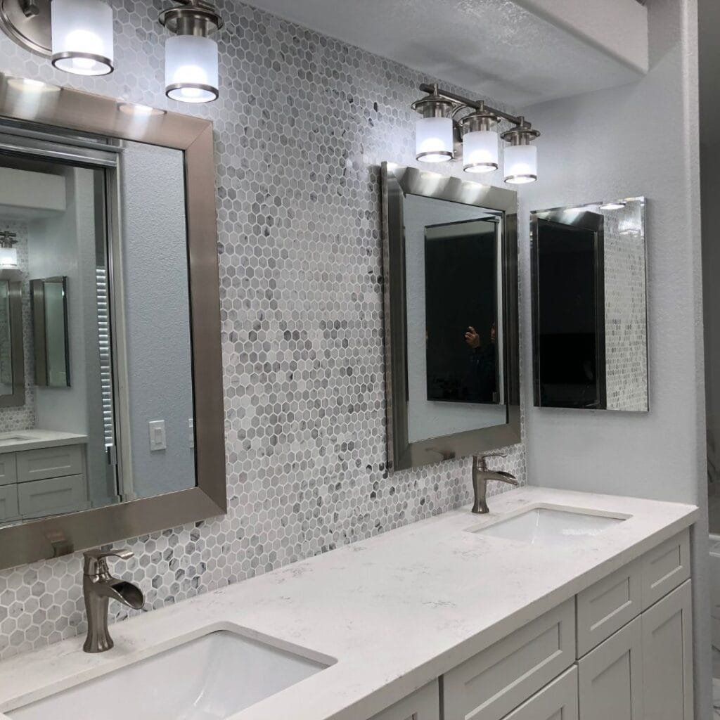 Bathroom with two sinks, mirrors, and a mosaic tile backsplash. White countertop and cabinets.