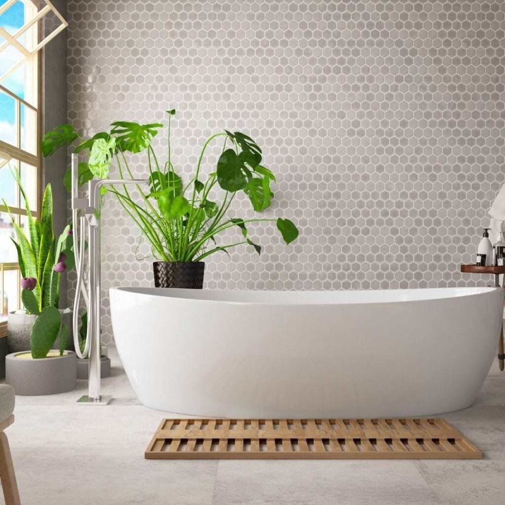 Modern bathroom with freestanding tub, potted plants, and light gray hexagon tile wall.