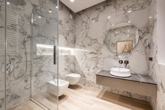 Luxurious bathroom with marble walls, glass shower, floating vanity, and round mirror.