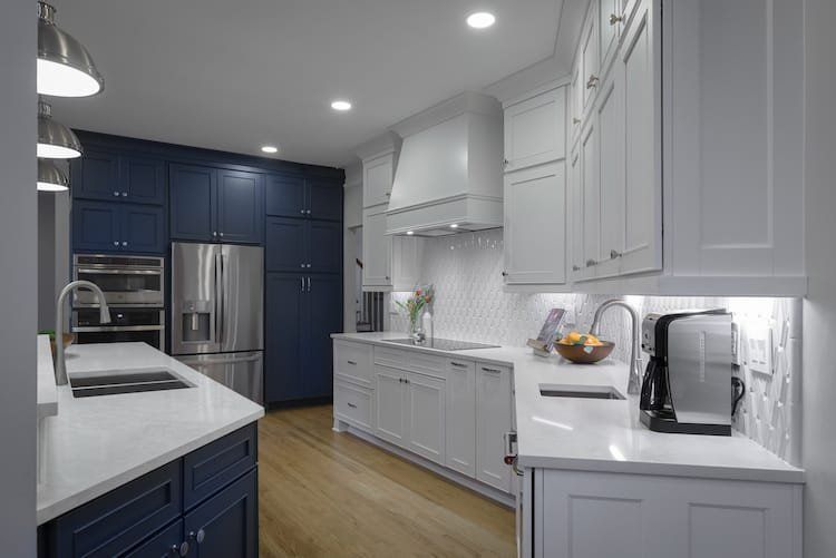 Modern kitchen with blue and white cabinets, stainless steel appliances, and white countertops.