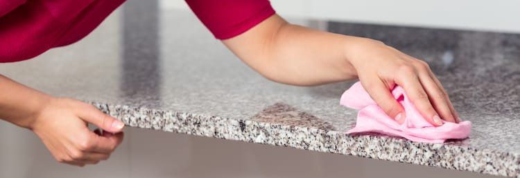 Person wiping a speckled countertop with a pink cloth.