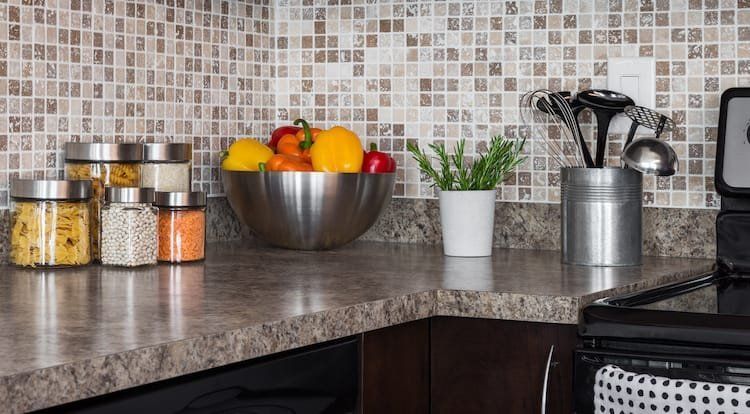 Kitchen counter with fruit bowl, jars of spices, utensils, and mosaic backsplash.