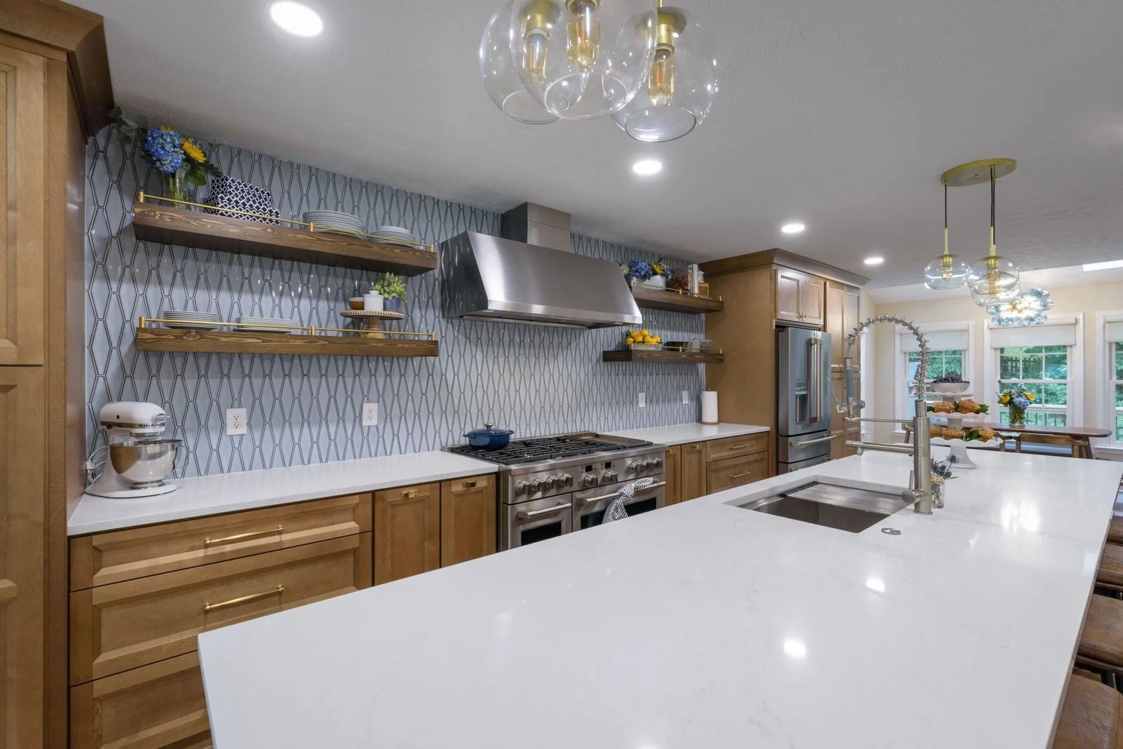 Modern kitchen with light wood cabinets, white countertops, blue backsplash, stainless steel appliances, and island with sink.