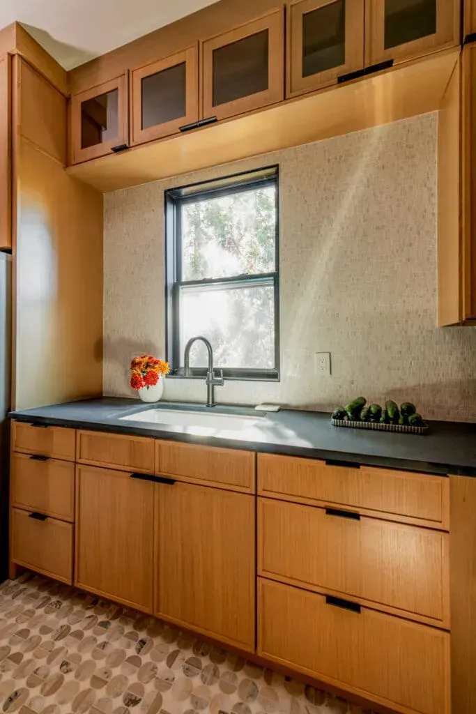 Wooden kitchen with dark countertops, cabinets, and a window above the sink.