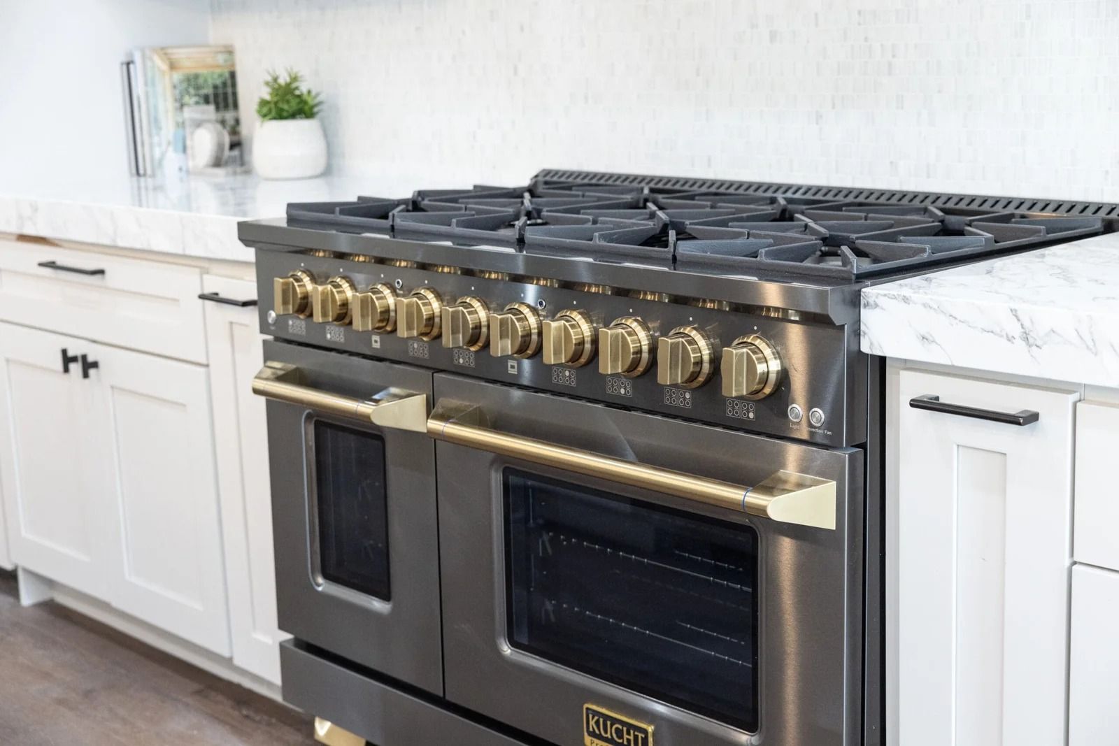 Stainless steel gas range with gold accents in a white kitchen.