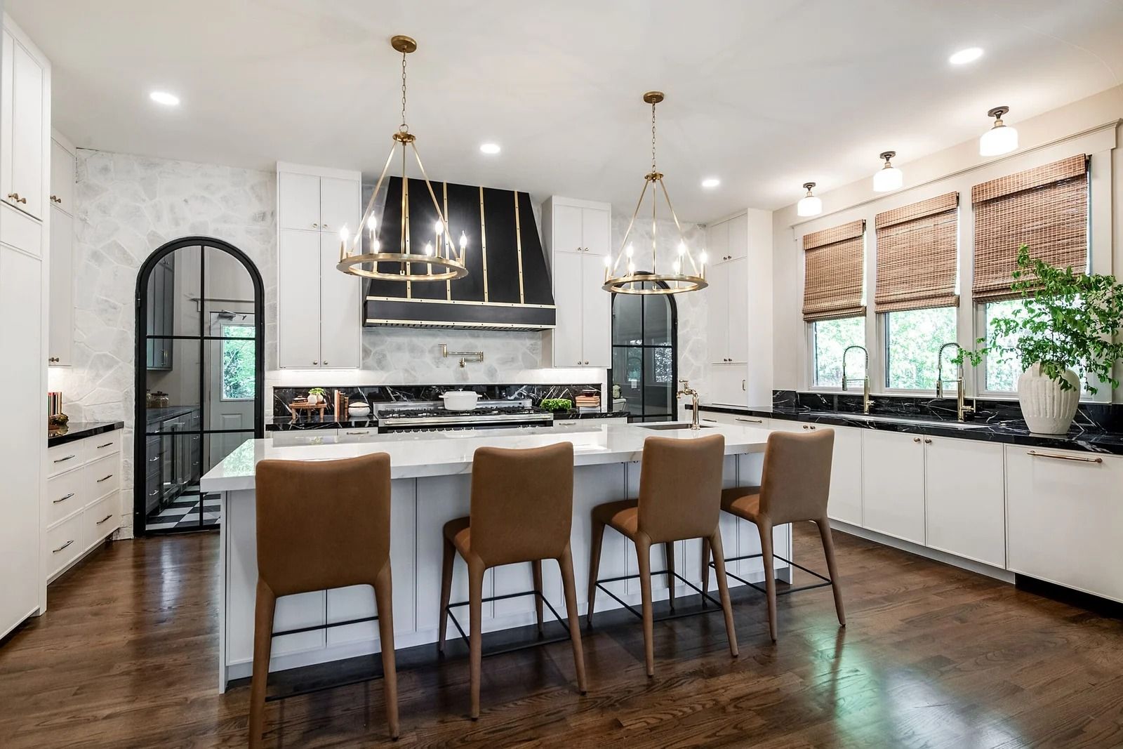 Modern white kitchen with island, brown barstools, black countertops, and gold light fixtures.