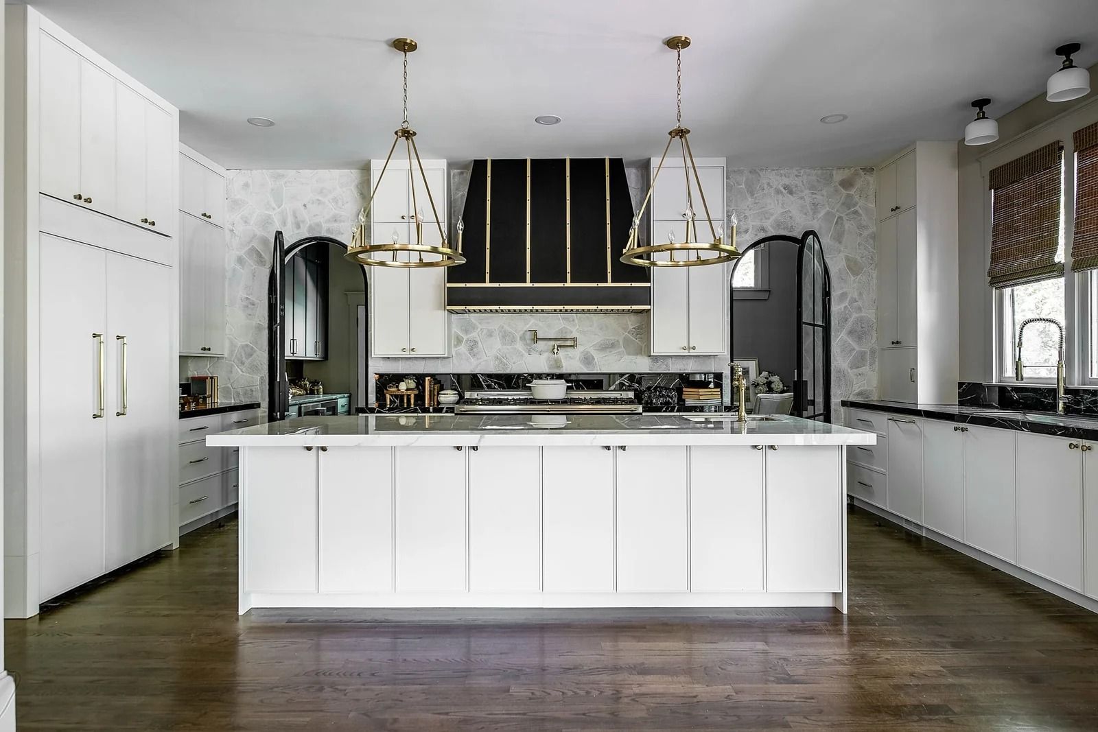 White kitchen with island, range hood, and pendant lights. Dark wood floors.
