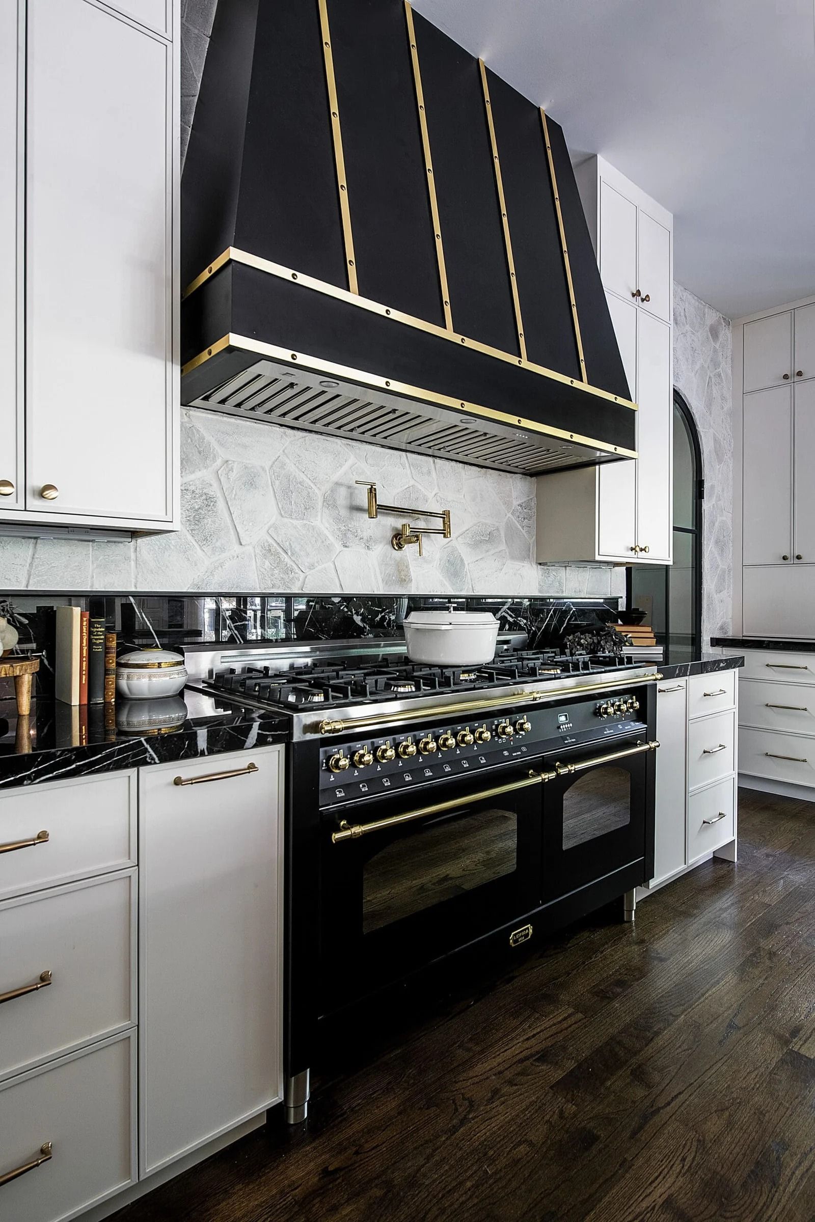 Black and white luxury kitchen with a black stove and range hood with gold accents.