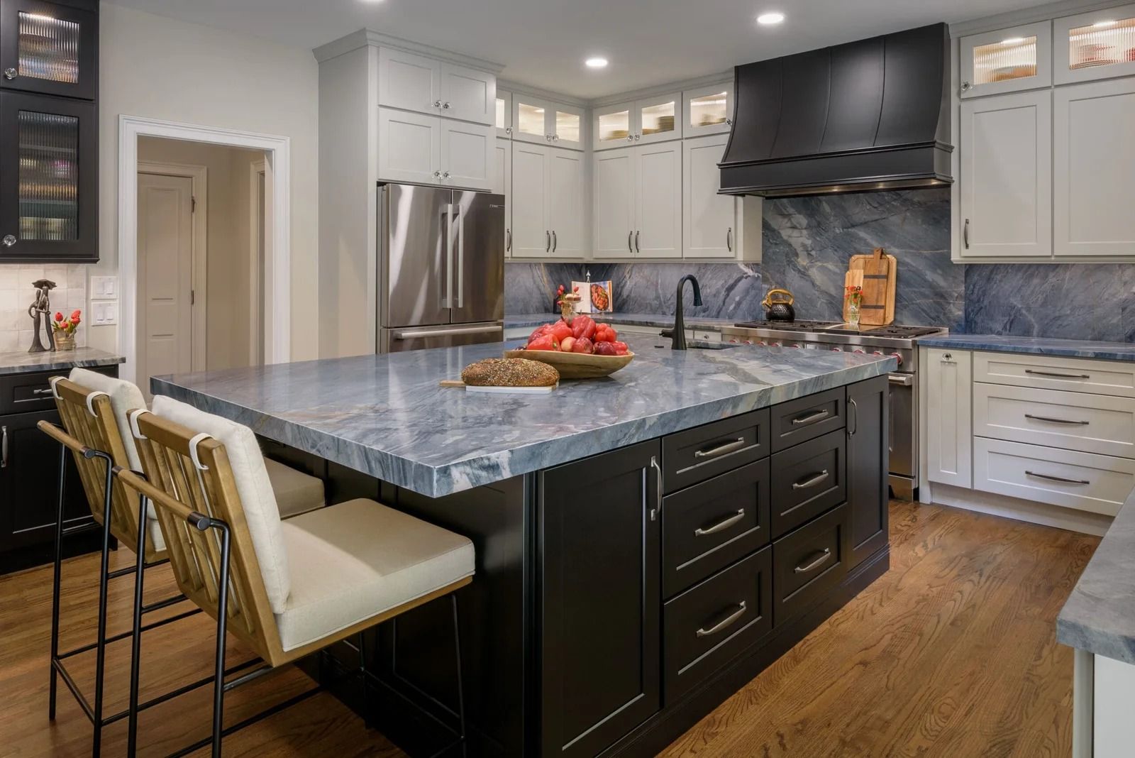 Modern kitchen with a dark island, light countertops, stainless steel appliances, and wood floors.