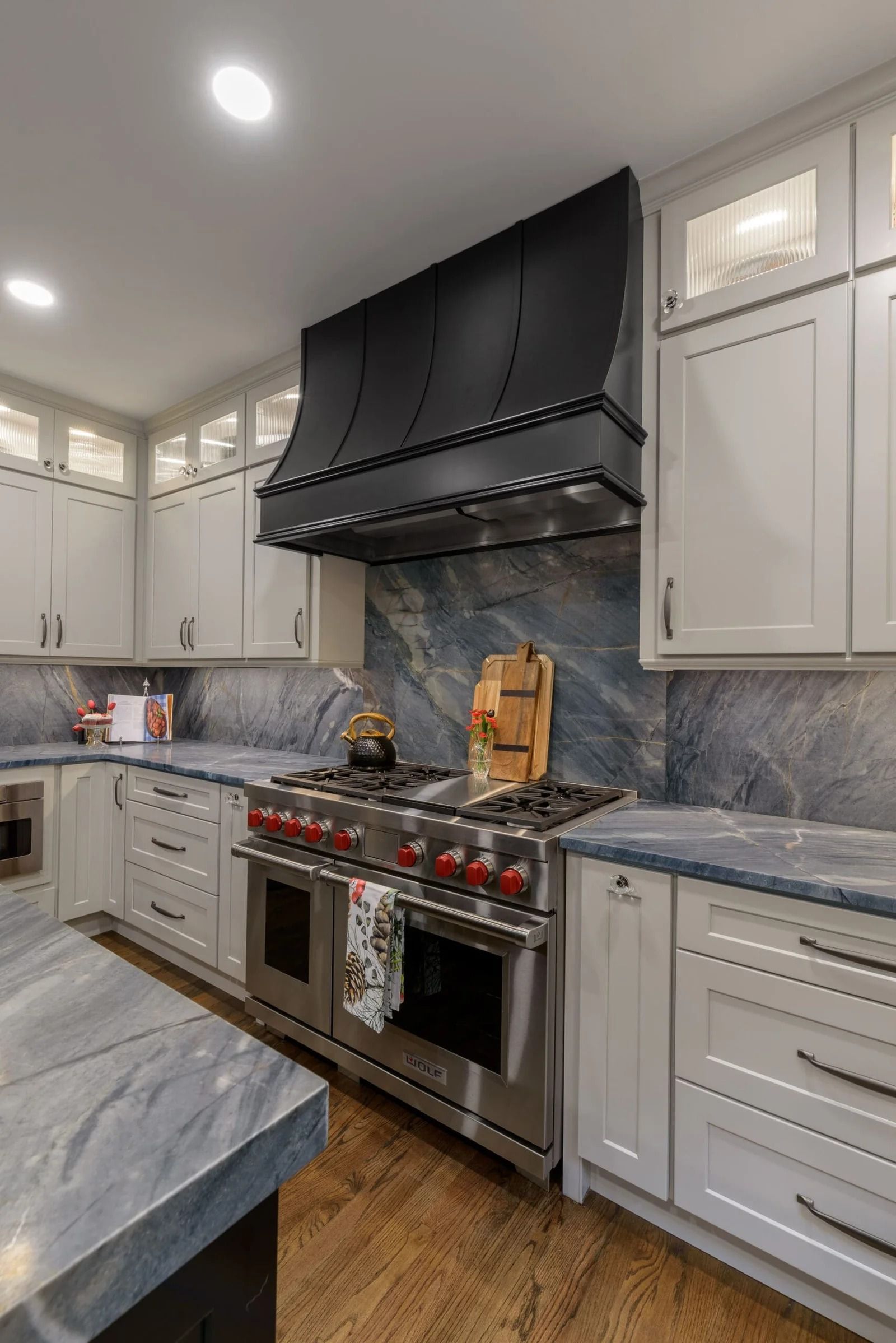 Kitchen with stainless steel range, black range hood, light cabinets, and blue countertops.