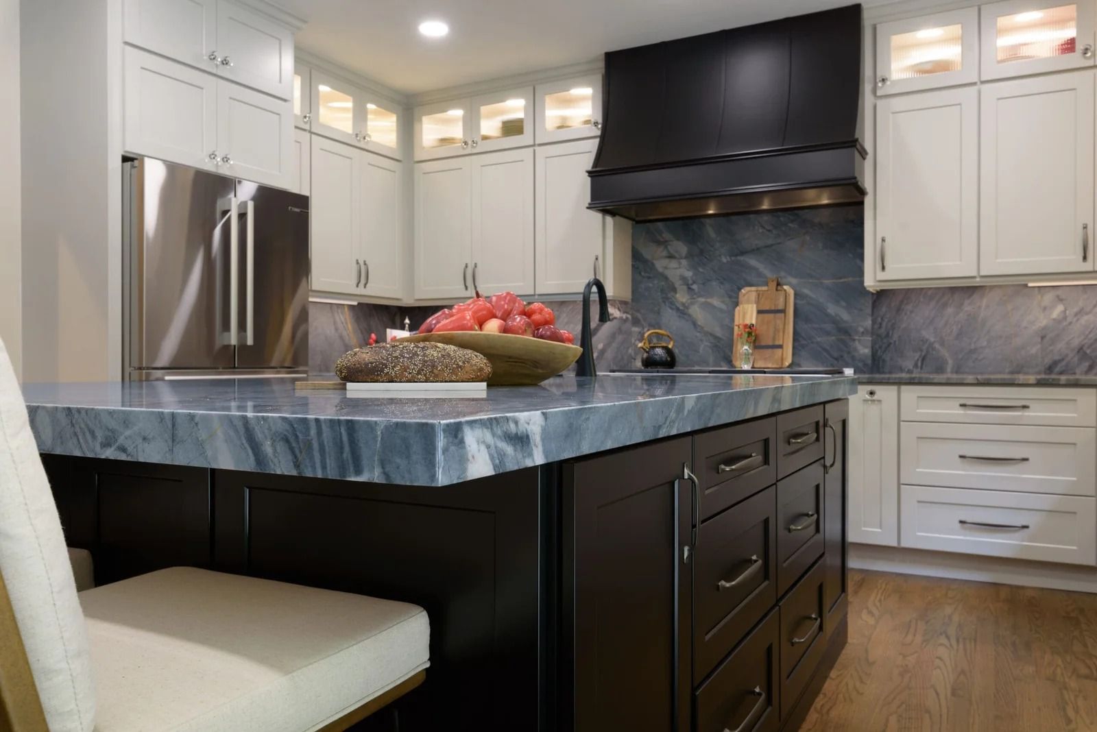 Kitchen with white cabinets, dark island, stainless steel fridge, and blue countertop.