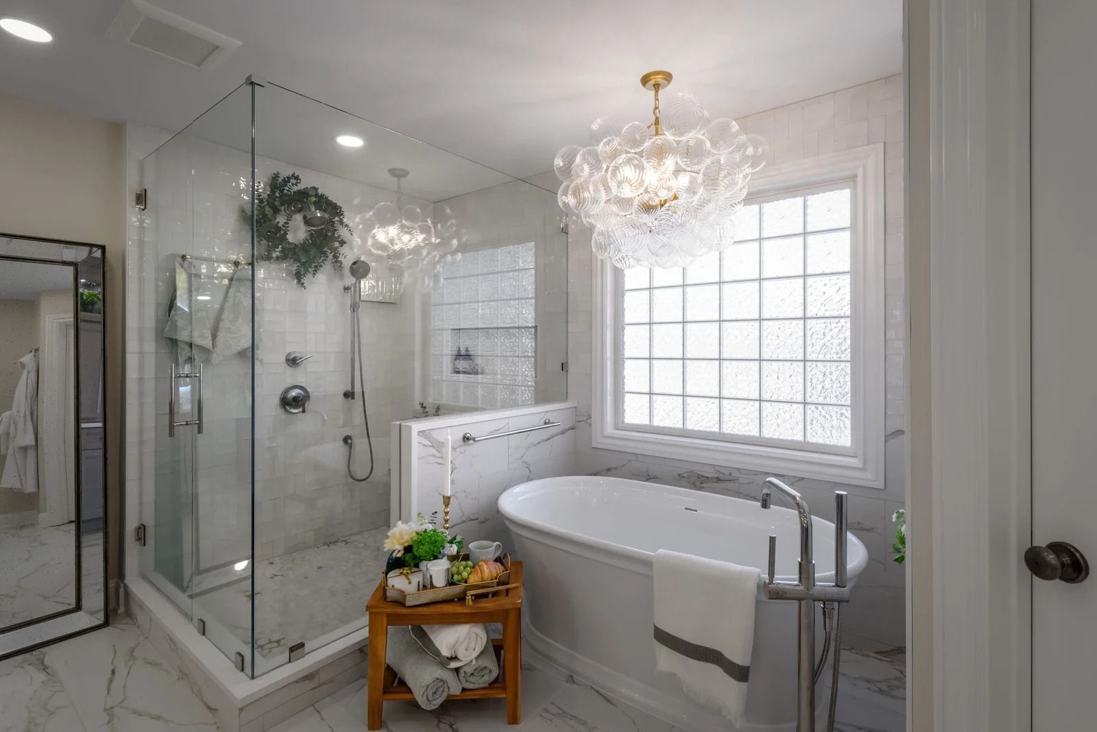 Modern bathroom with glass shower, freestanding tub, and a decorative chandelier.