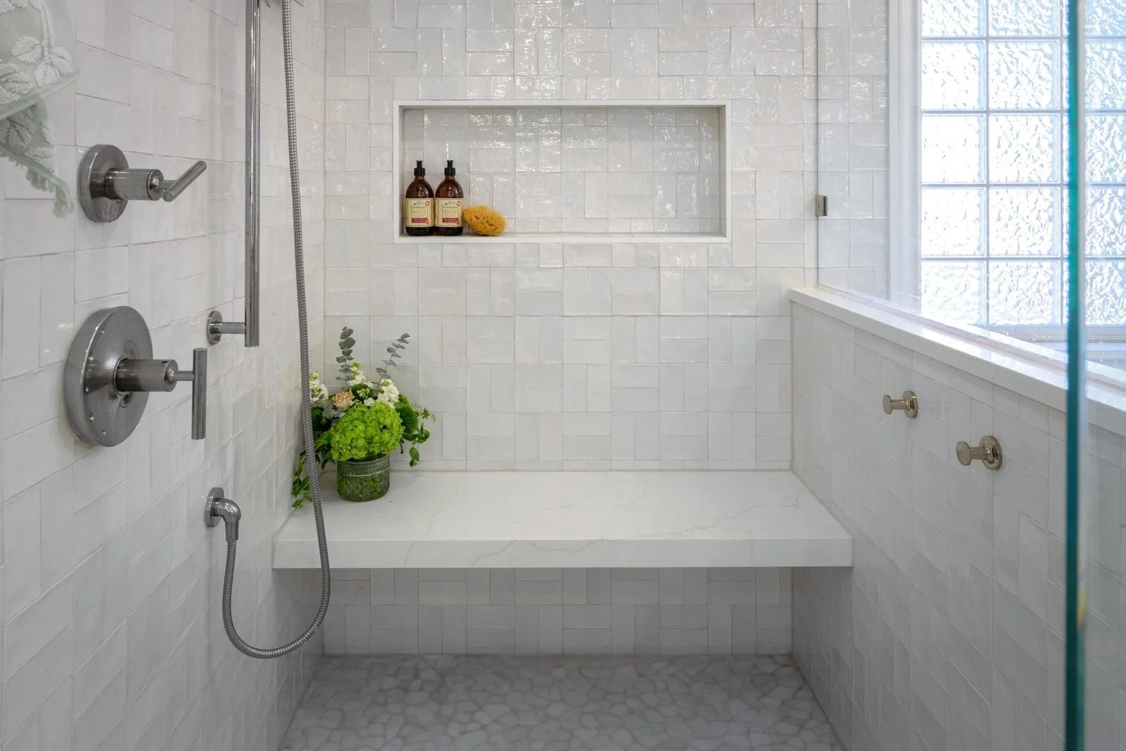 White tiled shower with built-in bench, shelf, and glass block window.