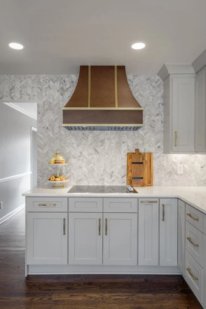 Modern kitchen with copper range hood, gray cabinets, and marble backsplash.