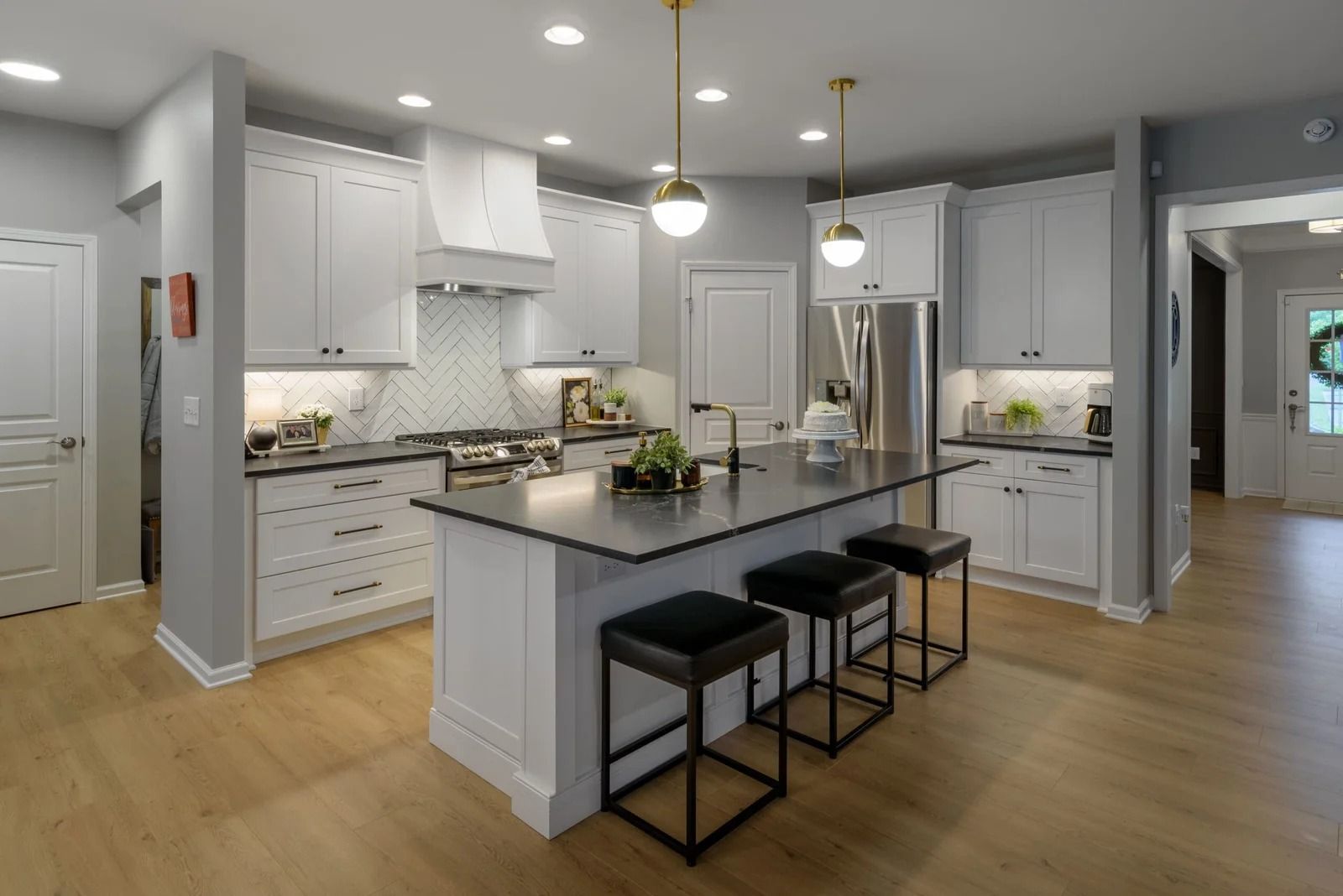 Modern white kitchen with island, stainless steel appliances, and wood flooring.