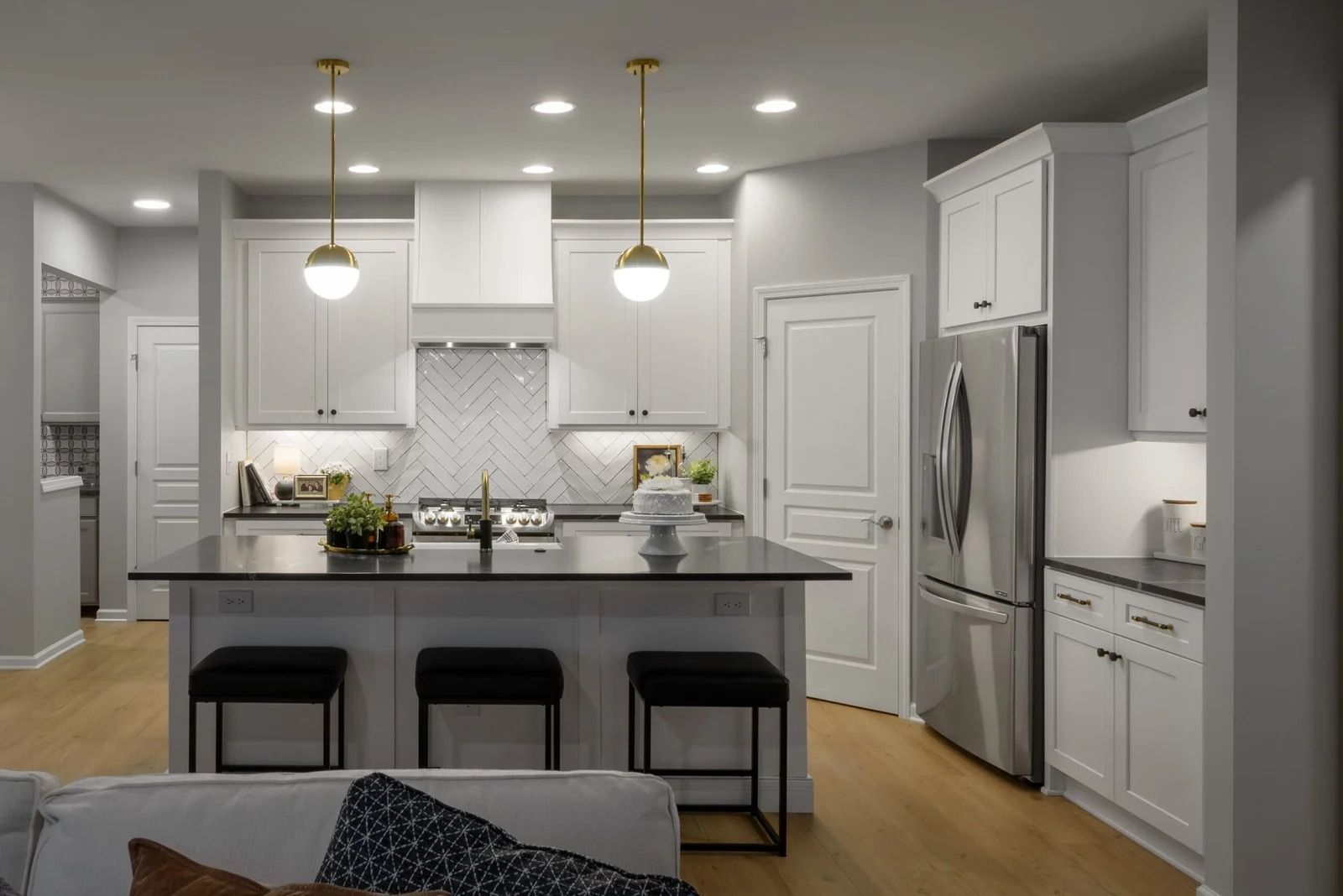 Modern kitchen with white cabinets, black island, stainless steel refrigerator, and wooden floors.