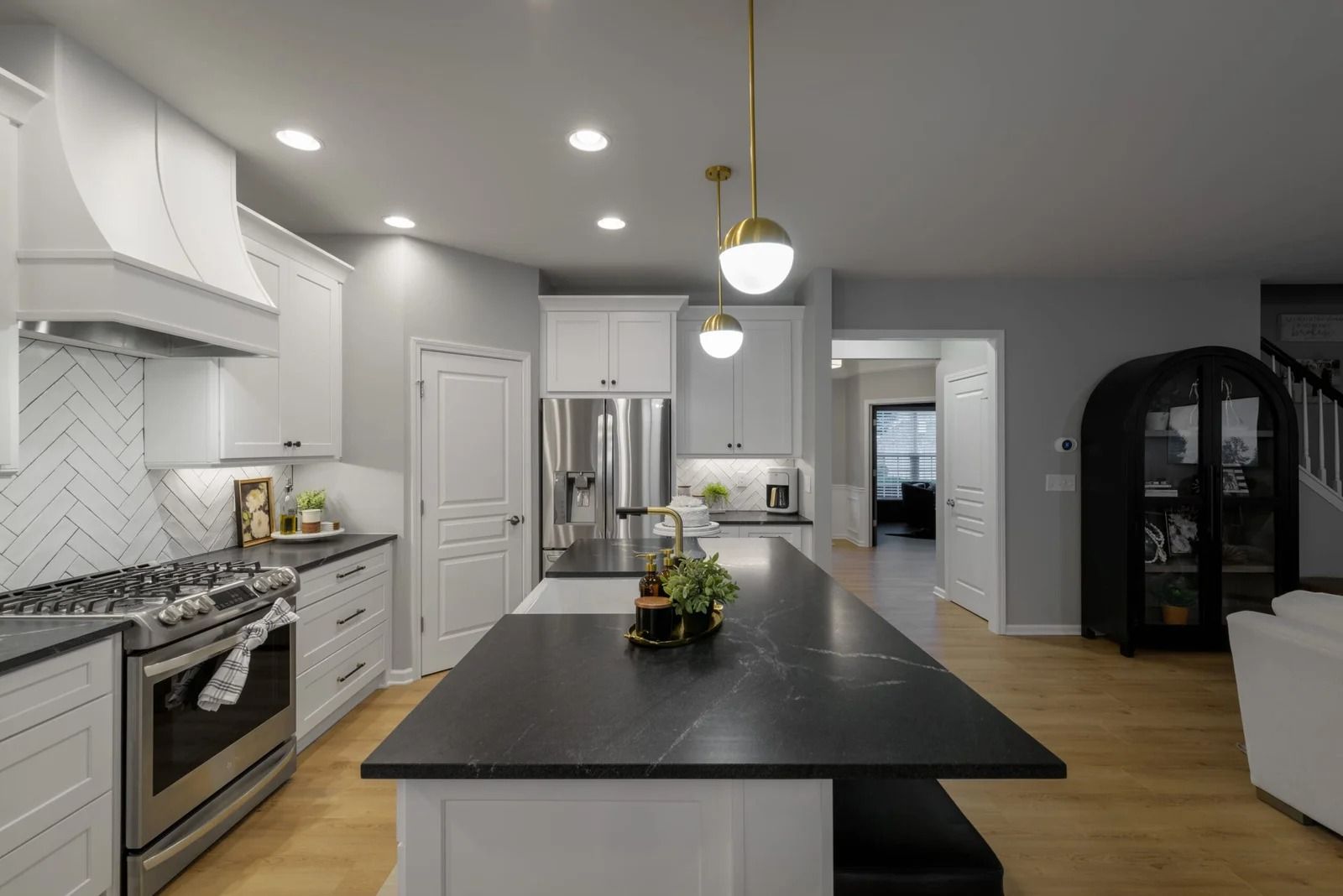 Modern kitchen with white cabinets, dark island countertop, and gold pendant lights.