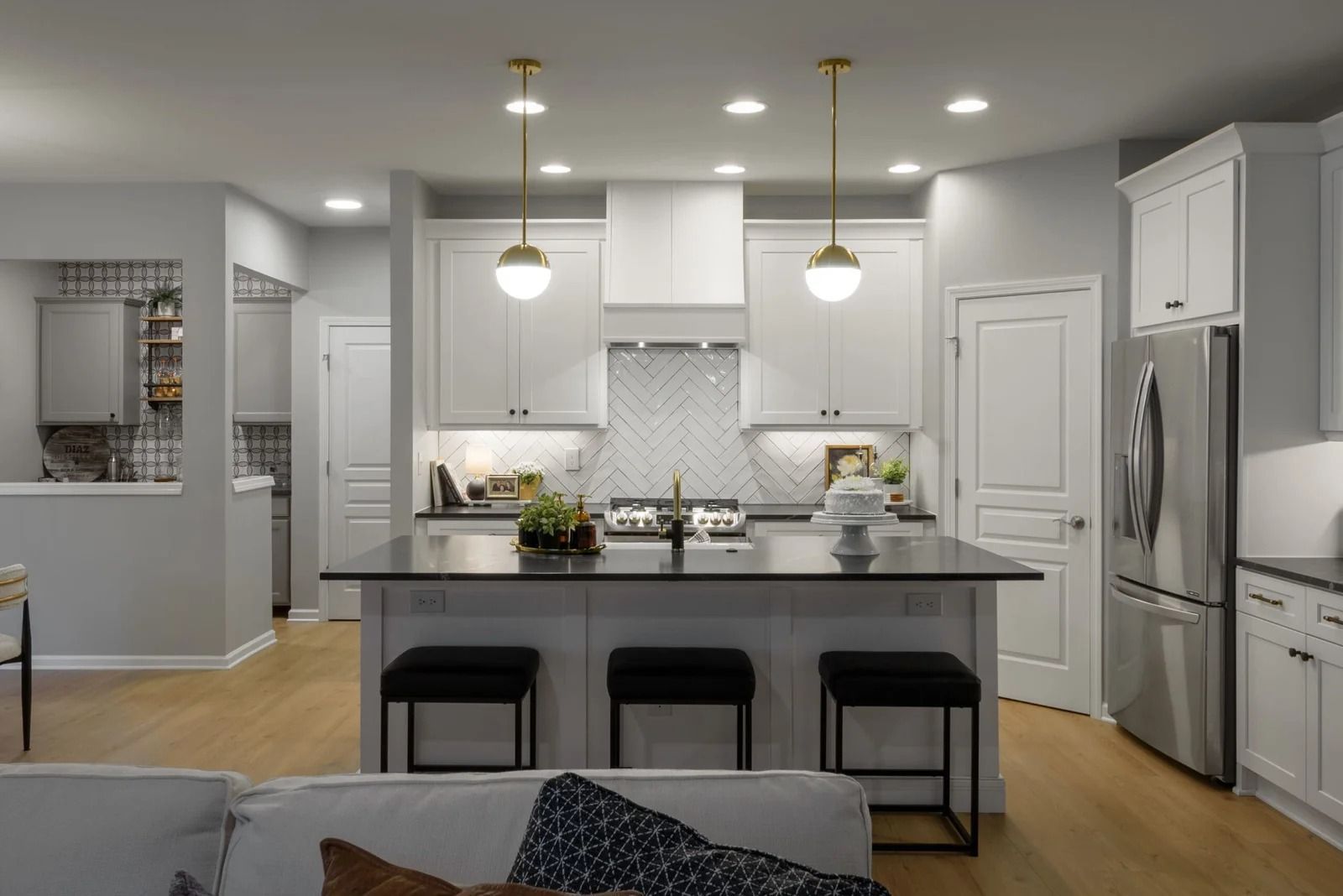 Modern kitchen with white cabinets, island with black countertop, stainless steel refrigerator, and gold pendant lights.