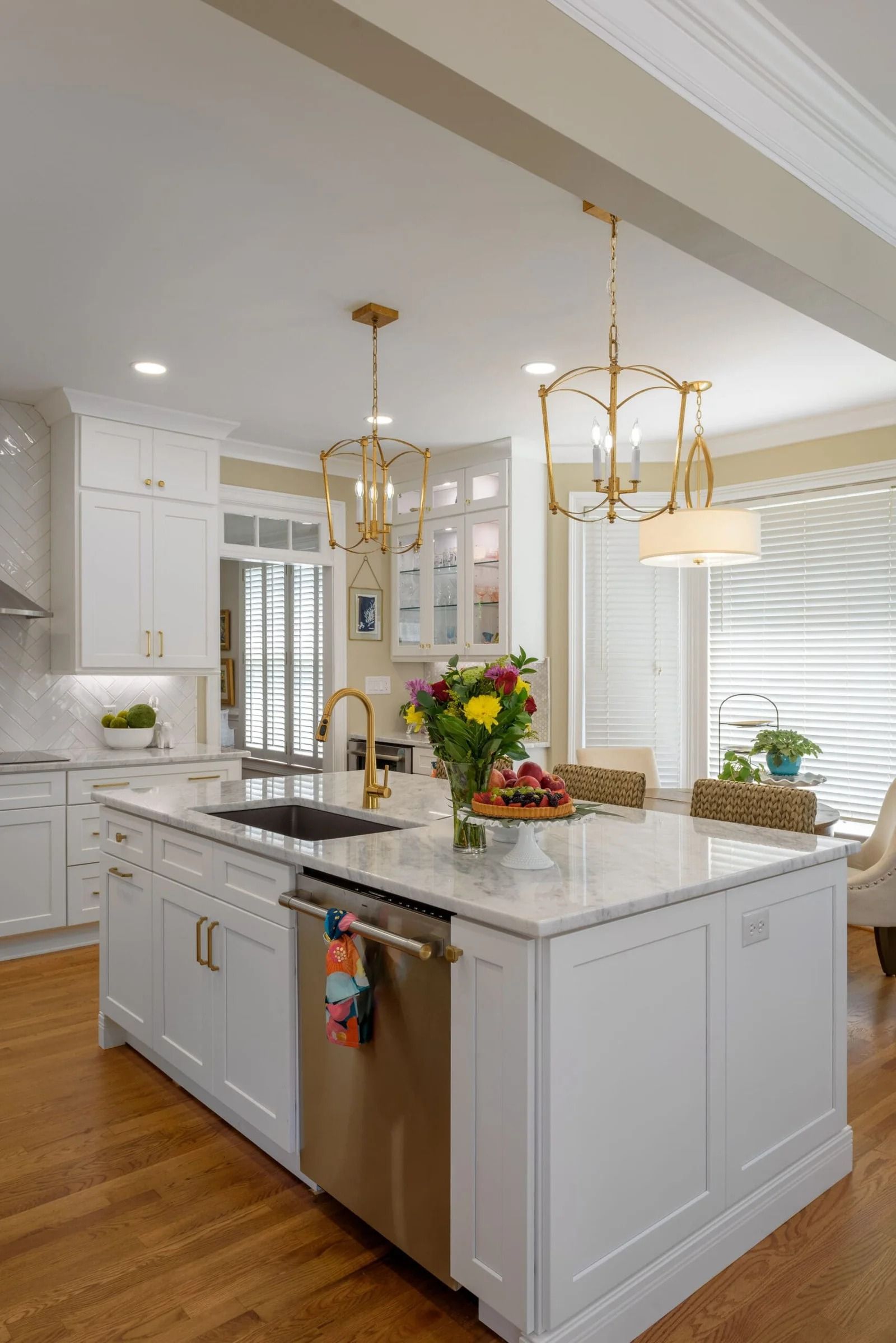 Bright kitchen with white cabinets, gold light fixtures, and a marble island.