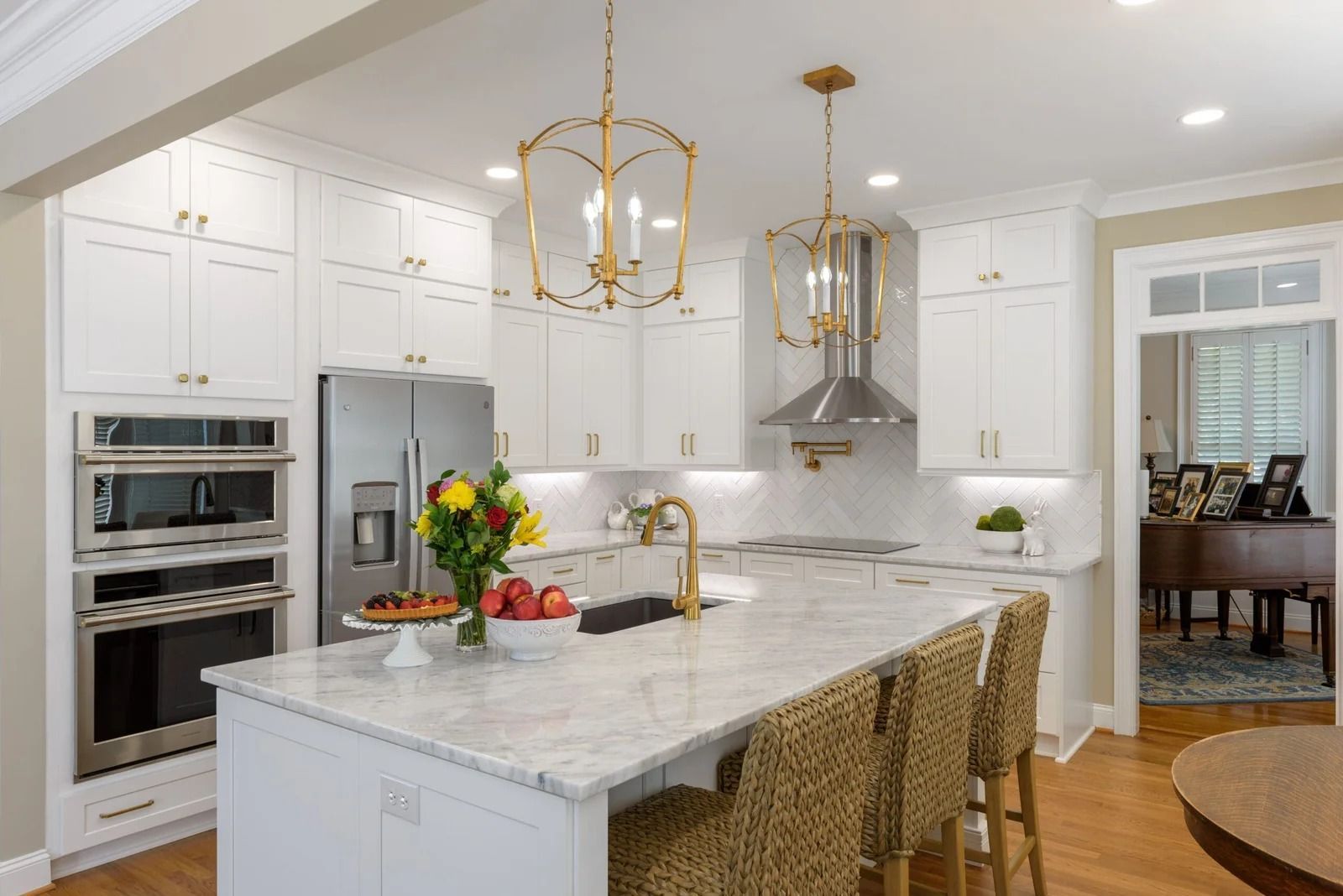 White kitchen with island, marble countertop, gold light fixtures, and woven bar stools.