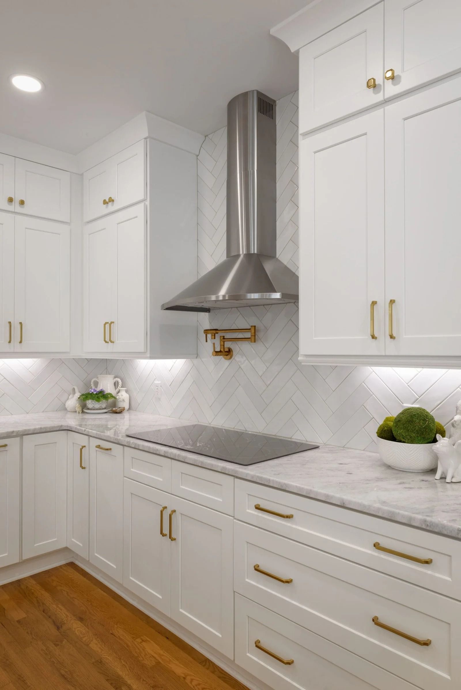 White kitchen with marble countertops, stainless steel range hood, and gold hardware.