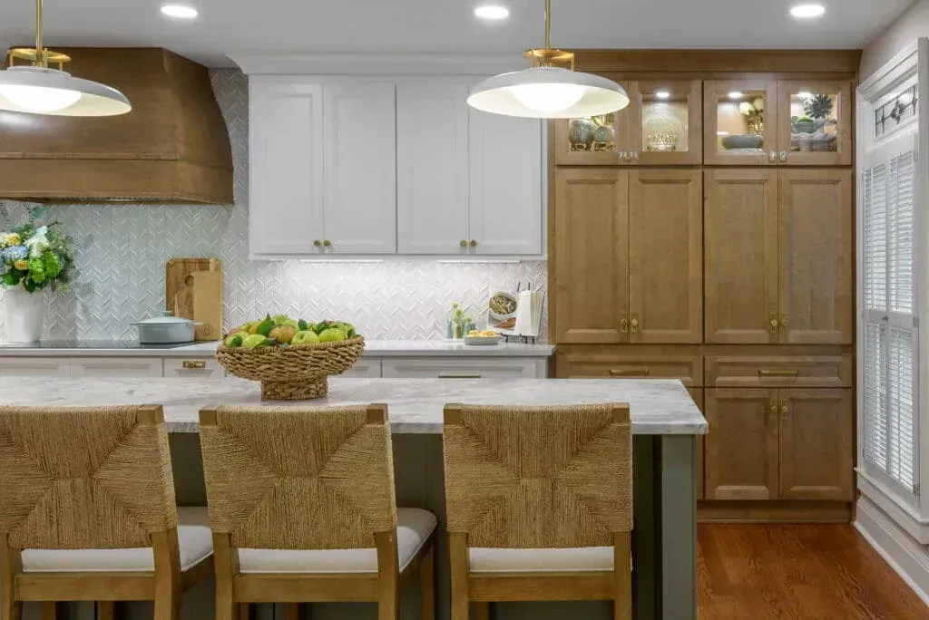 Kitchen with white and brown cabinets, island with woven chairs, gold light fixtures.