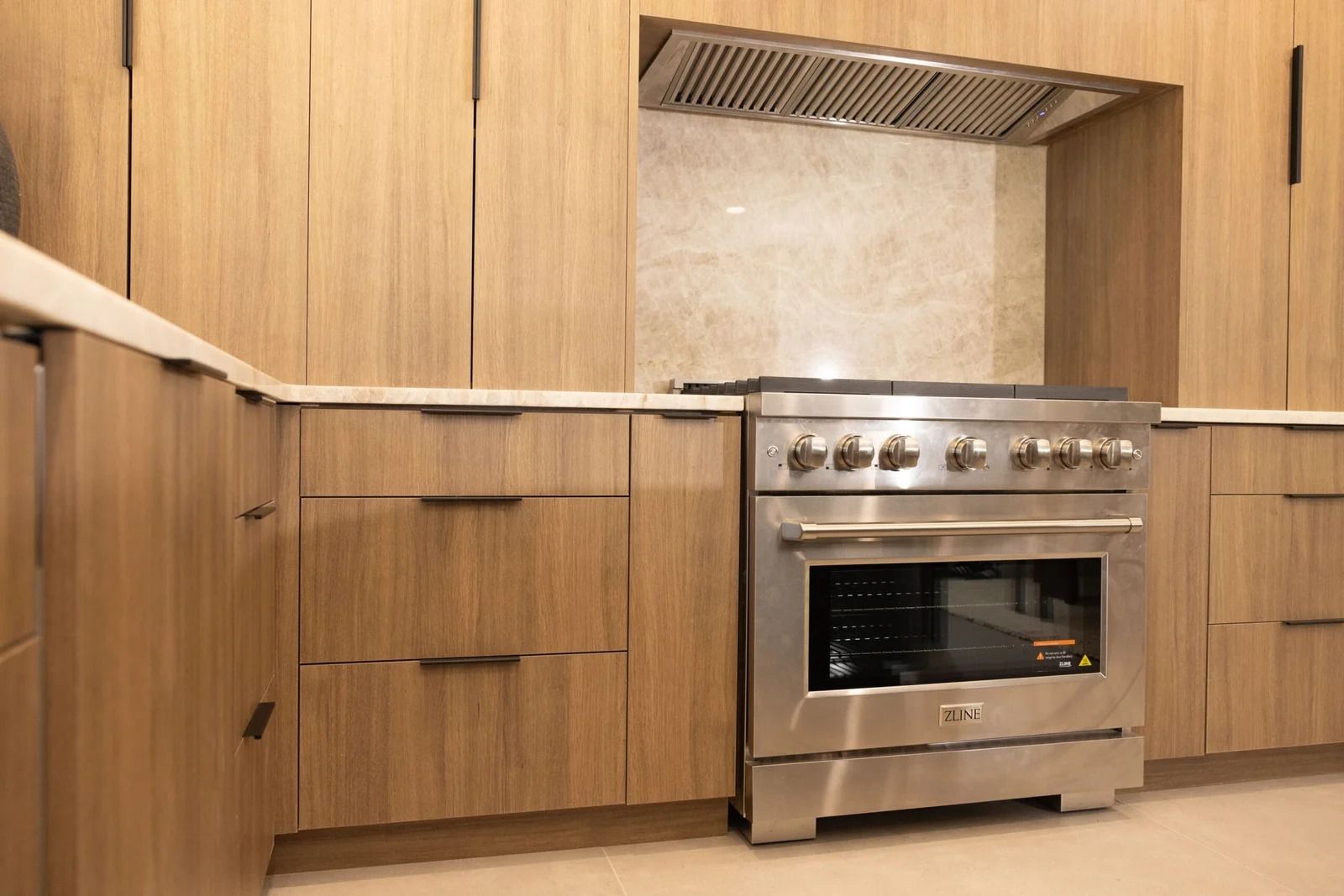 Modern kitchen with stainless steel stove, wooden cabinets, and white countertops.