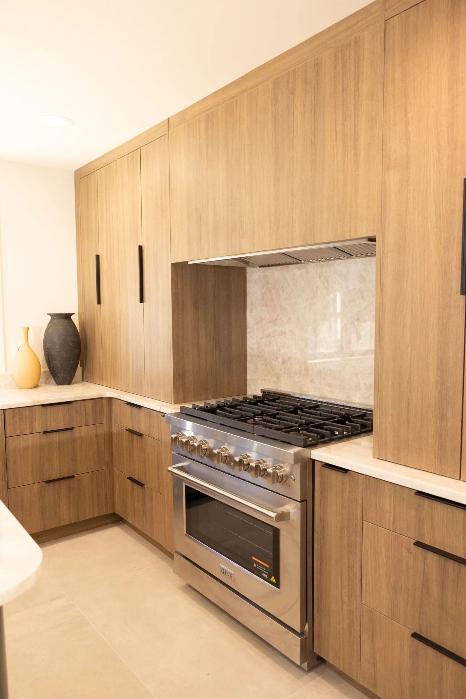 Kitchen with light wood cabinets, stainless steel range, and stone countertop.