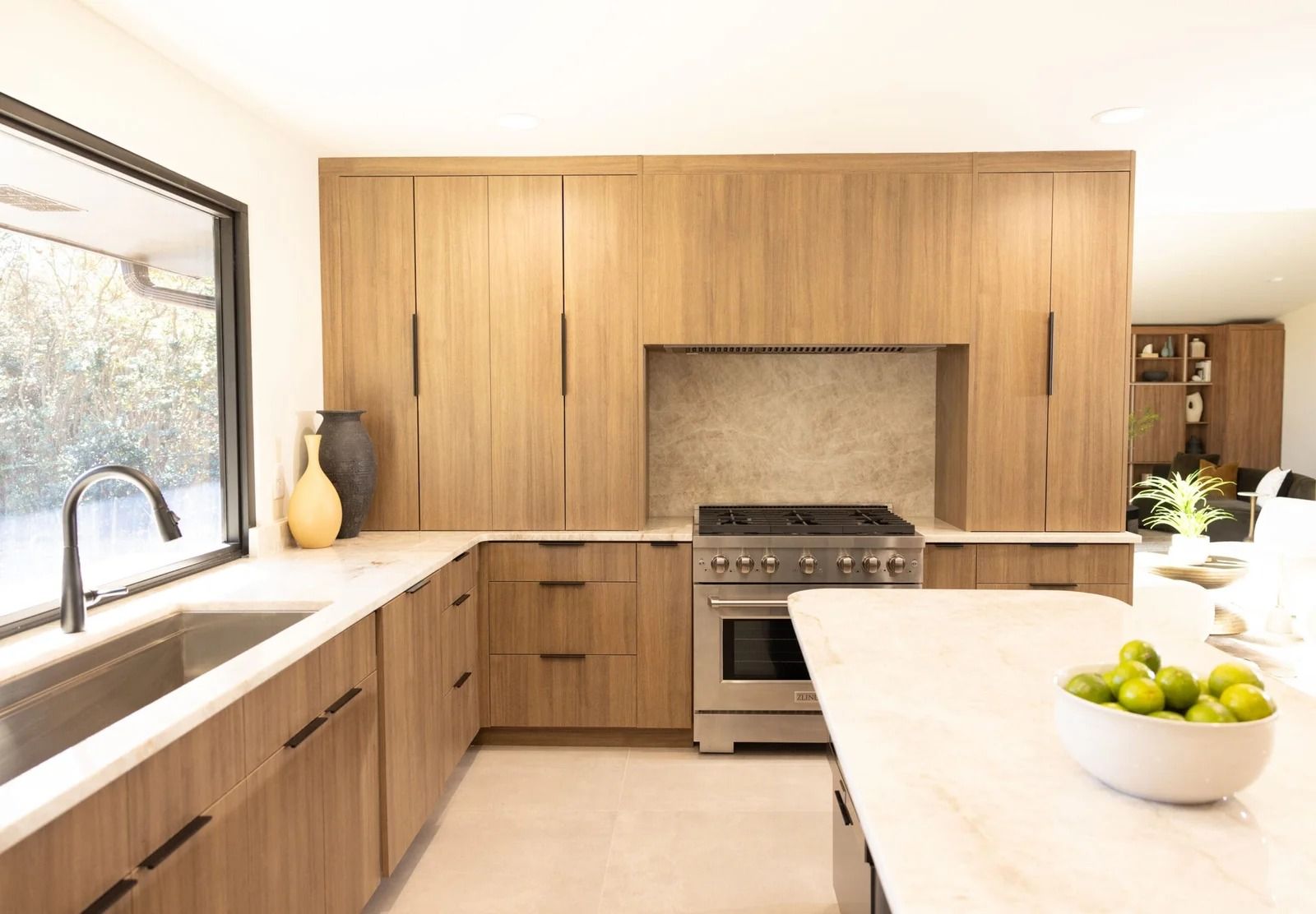Modern kitchen with light wood cabinets, stainless steel appliances, and a marble countertop.
