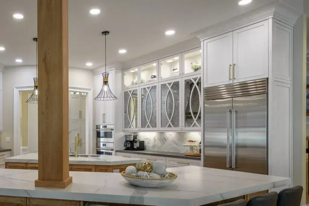 Spacious modern kitchen with white cabinets, large island, stainless steel refrigerator, and decorative glass-front cabinets.