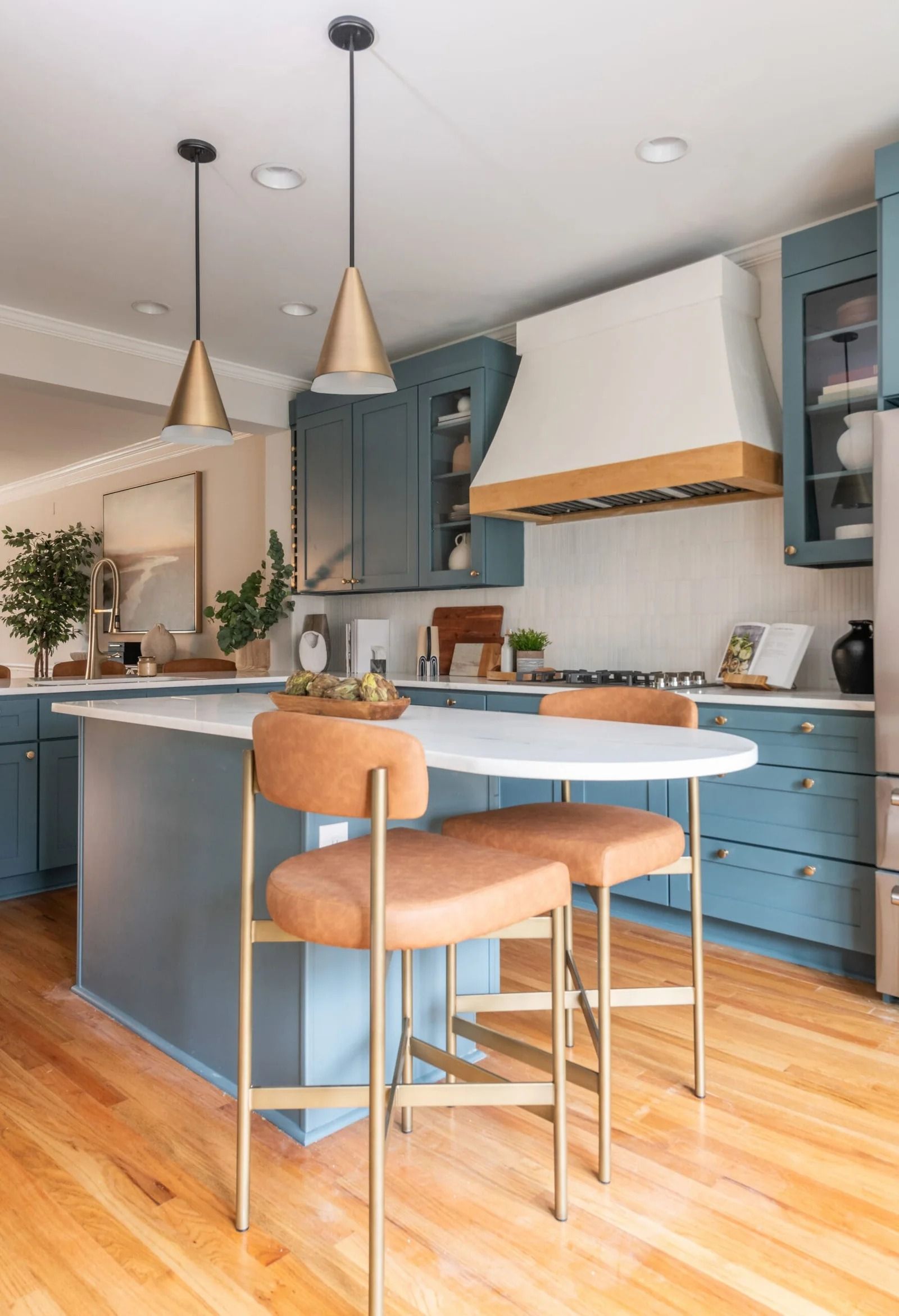 Blue kitchen with a white countertop island, gold pendant lights, and tan bar stools.