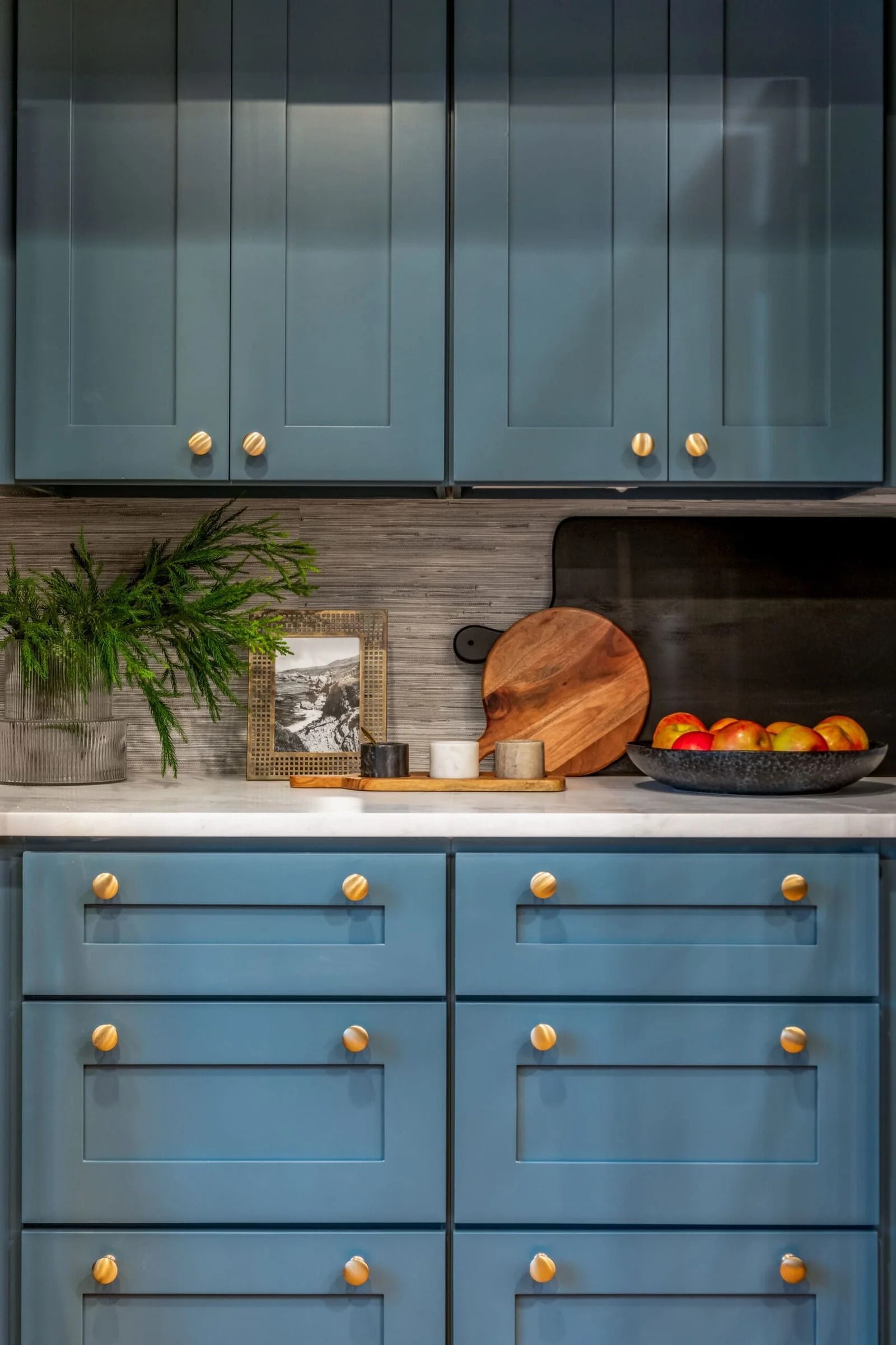 Blue kitchen cabinets with gold knobs, white countertops, and decorative items.