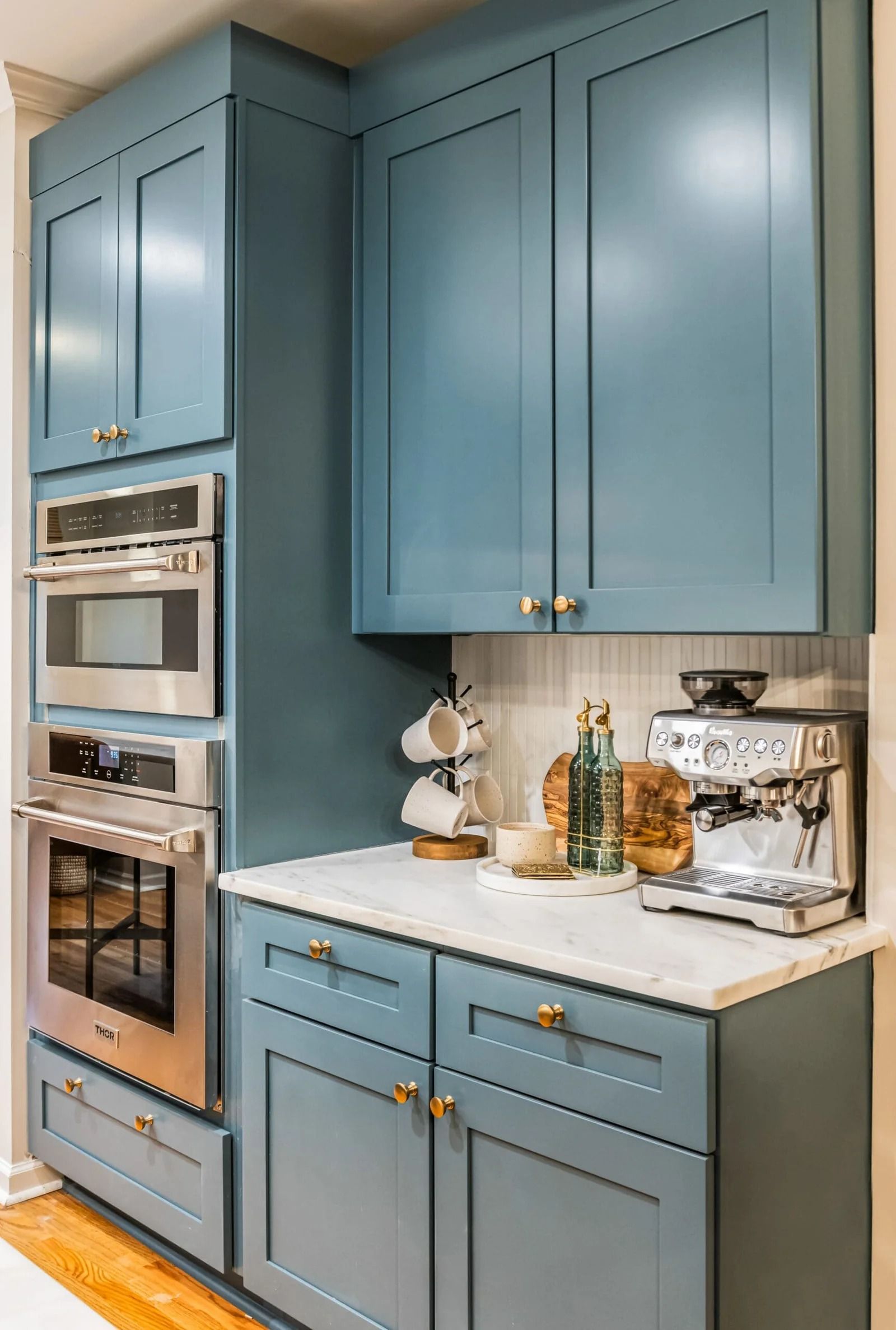 Blue kitchen cabinets with built-in ovens, marble countertop, and a coffee machine.