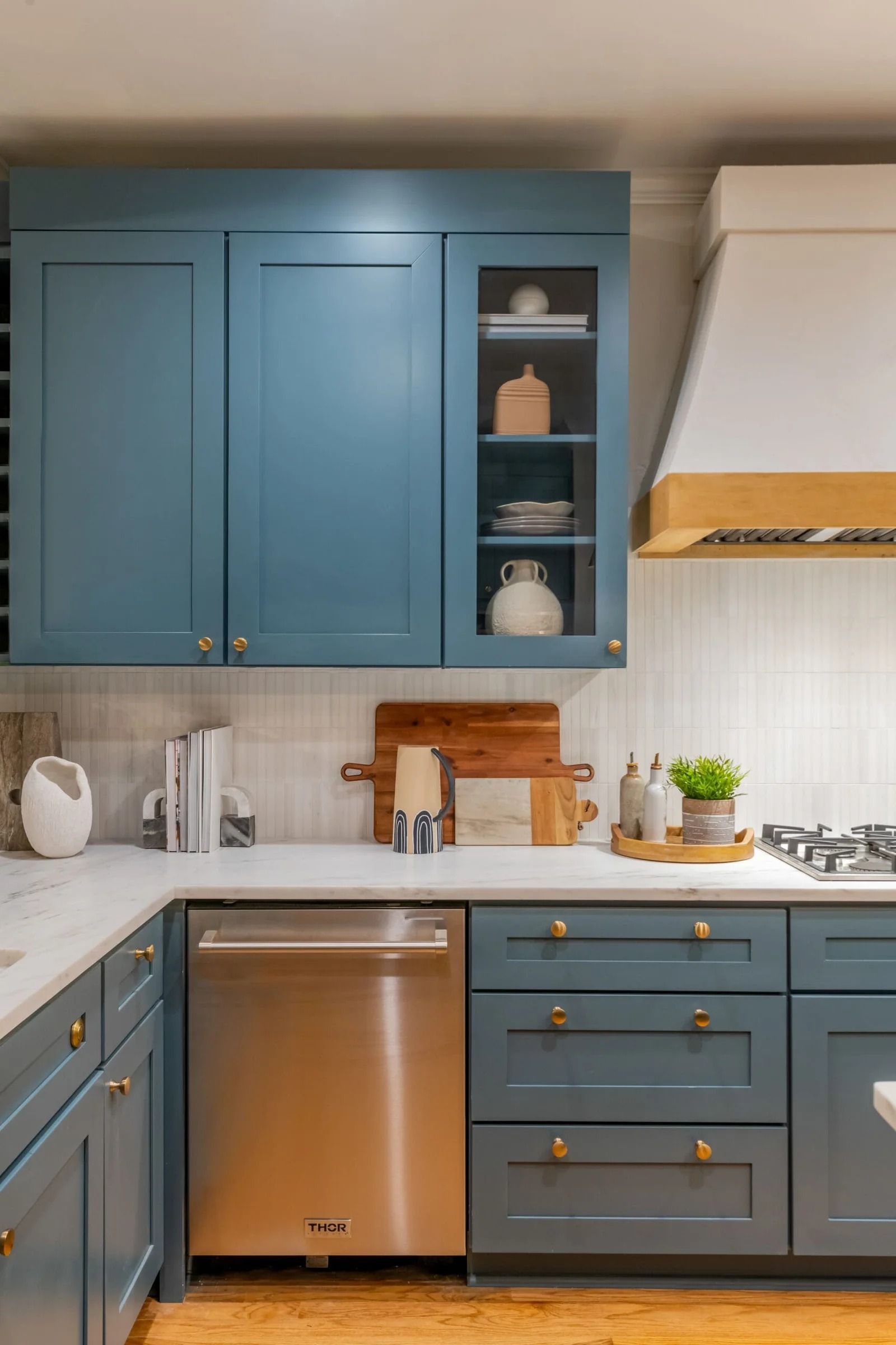 Blue kitchen cabinets, stainless steel dishwasher, white countertops, and white tile backsplash.