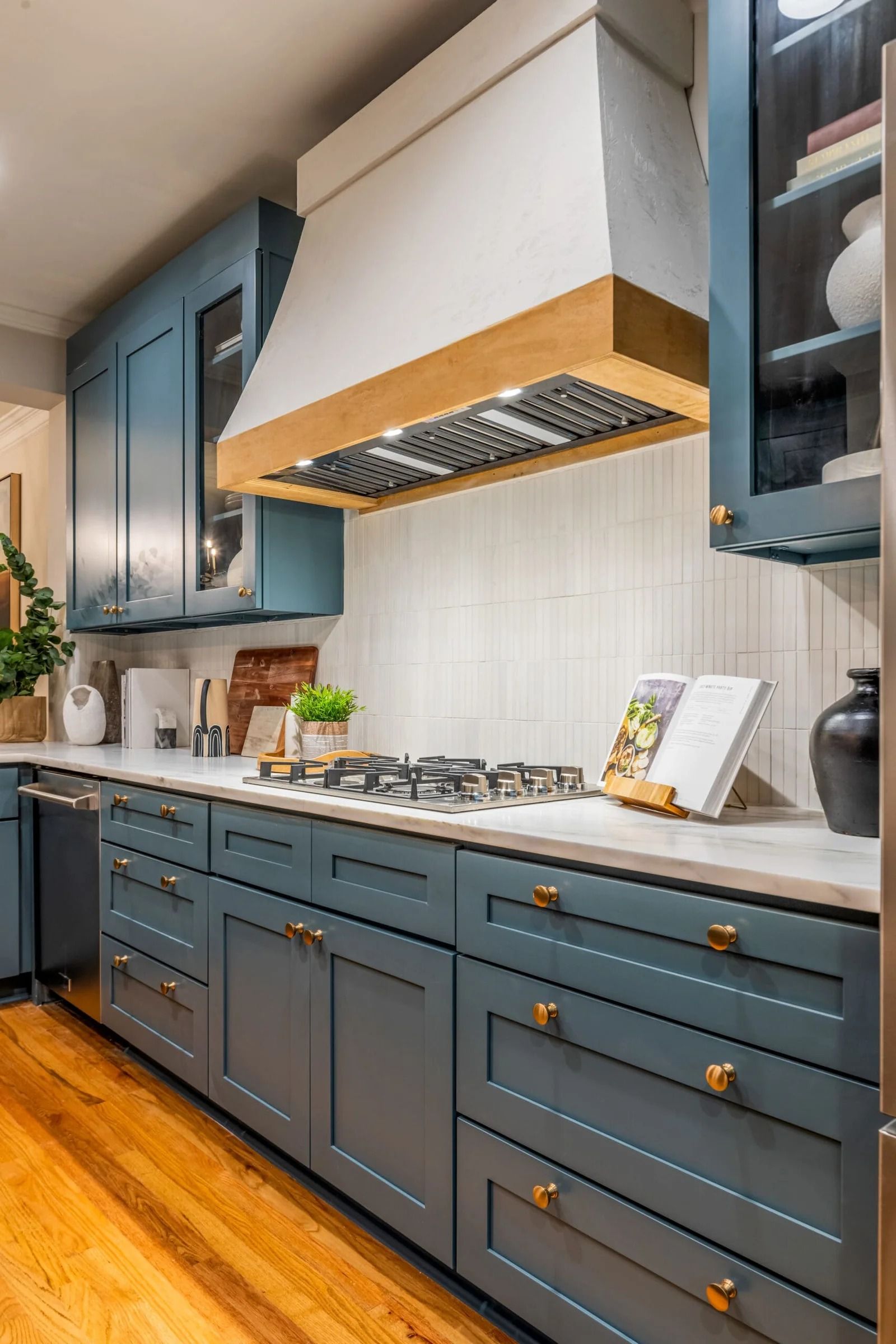 Blue kitchen cabinets with white countertops, a wood range hood, and a gas stove.
